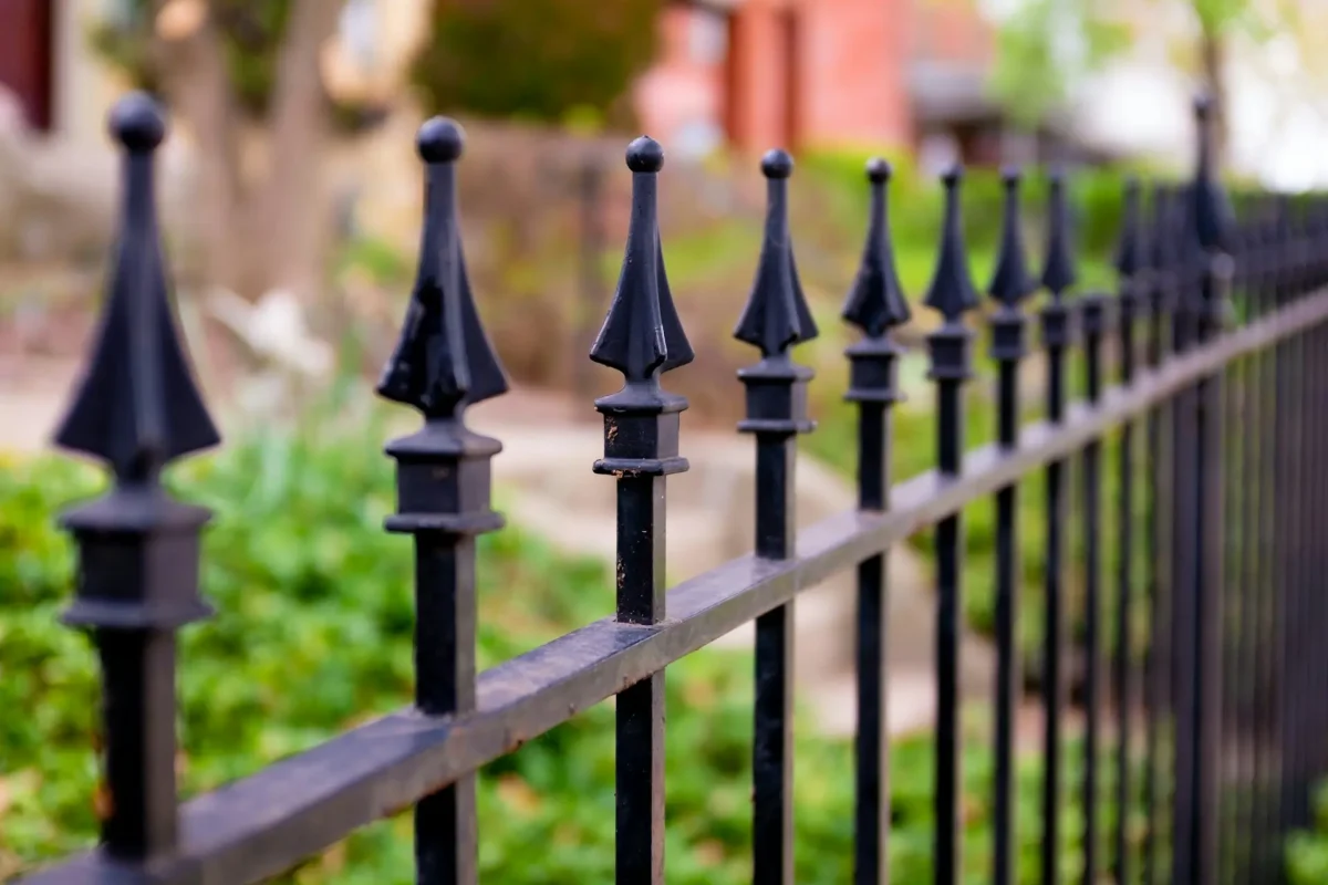 Close up of wrought iron fence in front of yard with stairs and grass