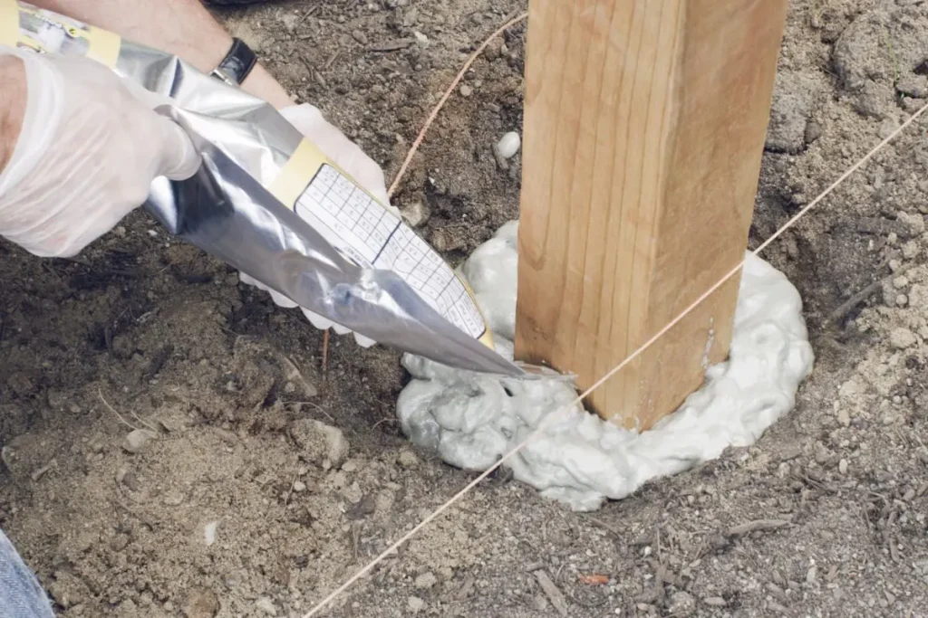 Pouring fence post foam around a wooden fence post.
